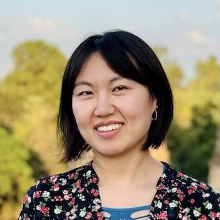an East Asian woman with short black hair and a floral shirt smiling in front of a background of trees
