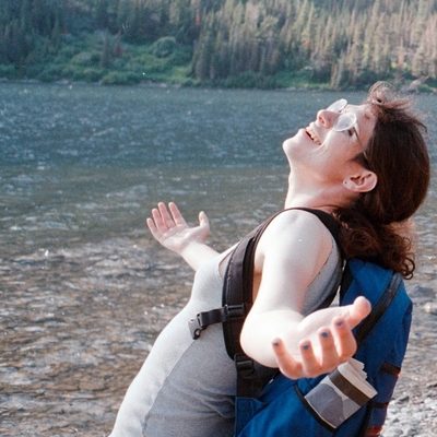 Izzy looking at the sky with arms outstretched, a lake in the background