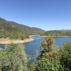 photo of a lake in front of some green hills with trees in the foreground