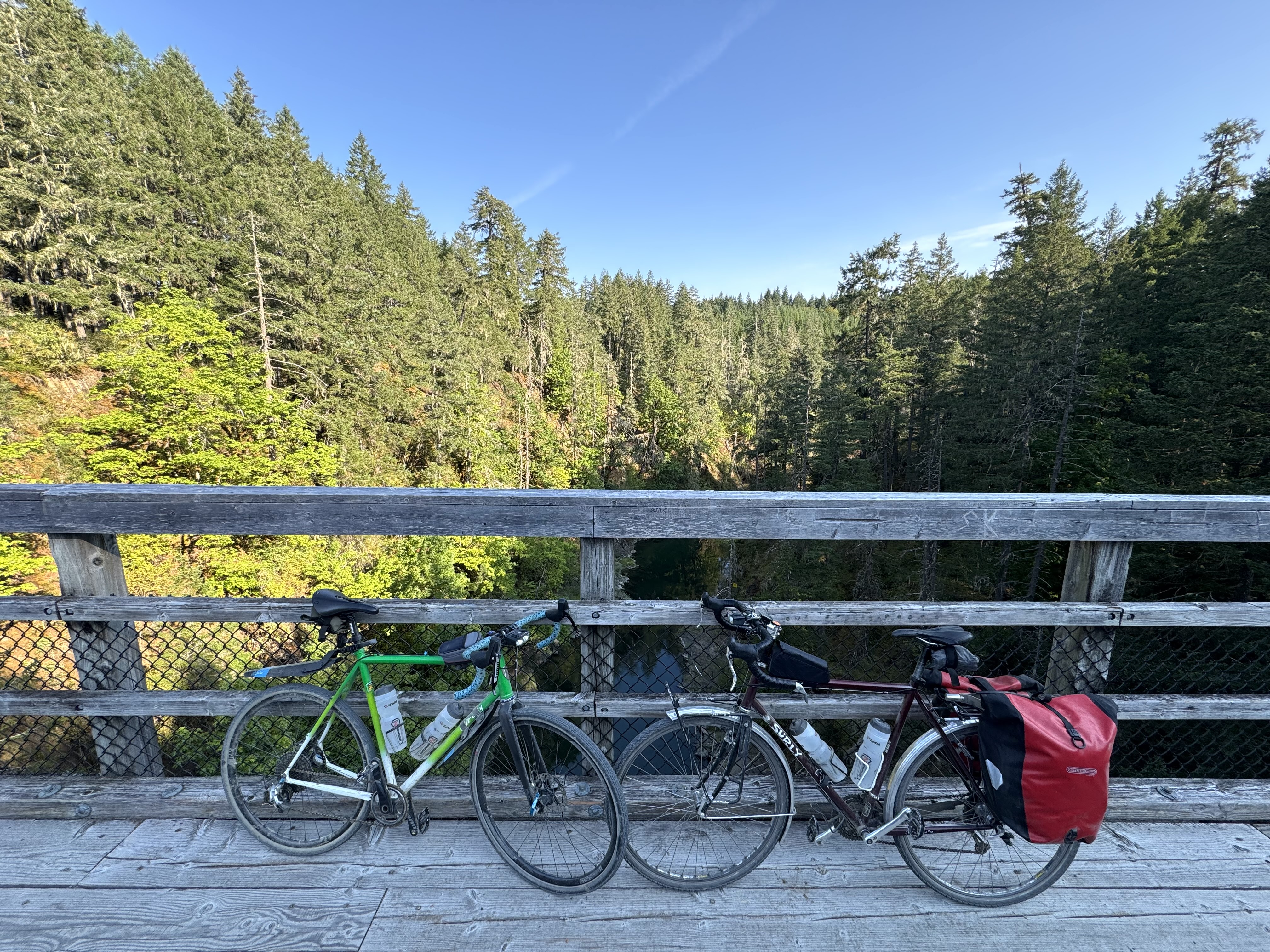two bikes on a wood bridge over a river with forest all around